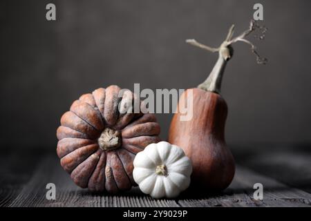 Drei verschiedene Kürbisse auf Holztisch auf dunkelbraunem Hintergrund Stockfoto