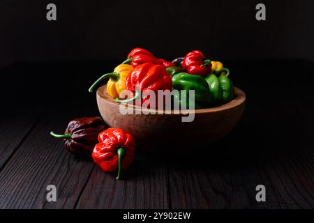 Gereifte mehrfarbige Habanero-Paprika (Paprika chinense) in einer Holzschale auf rustikalem Tisch. Sehr heiße mexikanische Paprika aus der Nähe Stockfoto