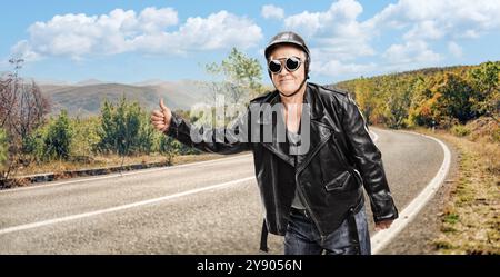 Reifer Anhalter in schwarzer Lederjacke und Helm auf der Straße Stockfoto