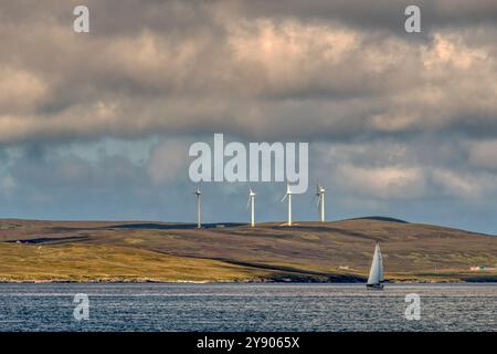 Yacht, die an den Windturbinen der Garth Wind Farm auf Snevlabreck, nördlich von Gutcher auf Yell, Shetland Islands, vorbeisegelt. Von der Insel Fetlar aus gesehen. Stockfoto