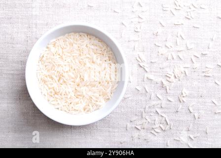 Weißer Basmatireis, in einer weißen Schüssel auf Leinenstoff. Lange und schlanke Körner mit aromatischem Geruch und Geschmack. Reiskörner einer Sorte Oryza sativa. Stockfoto