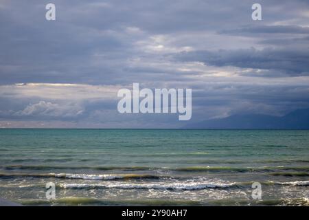 Hellgrüne Farbe des Ionischen Meeres. Albanische Berge am Horizont. Intensiver bewölkter Himmel im Spätsommer. Acharavi, Korfu, Griechenland. Stockfoto