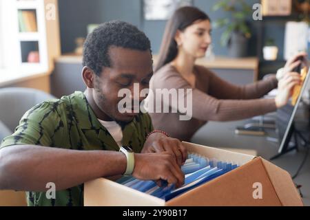 Porträt eines lächelnden afroamerikanischen Mannes, der Dokumente im Ordnerkarton im Büro durchsucht, im Kopierraum Stockfoto