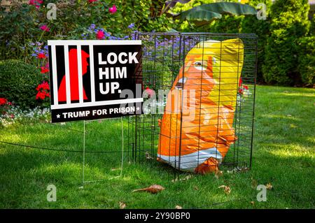 Eine Präsidentschaftswahlanzeige 2024 mit einem Anti-Donald Trump-Schild und einer leuchtend orangen aufblasbaren Figur von Trump in einem Käfig. Stockfoto