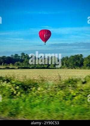 Roter Heißluftballon, schwebt tief über grünem Feld. Stockfoto