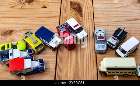 Eine Sammlung von Spielzeugfahrzeugen, darunter Polizeiautos, Krankenwagen und Feuerwehrwagen, die auf einer Holzplatte angeordnet sind Stockfoto