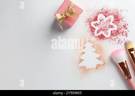 Weihnachtsdekorationen aus Puder und Rouge, Geschenkbox und Make-up-Pinsel auf weißem Hintergrund, flach gelegt. Leerzeichen für Text Stockfoto