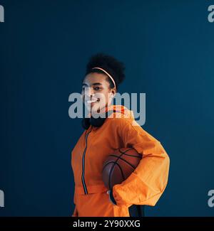 Professioneller Basketballspieler in oranger Sportbekleidung posiert im Studio vor blauem Hintergrund professioneller Basketballspieler in oranger Sportbekleidung Pose Stockfoto