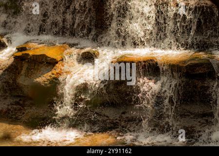 Das kaskadierende Wasser fließt über eine Reihe von Felsen und schafft eine ruhige und dynamische Szene. Das Sonnenlicht strahlt aus dem Wasser und unterstreicht die natürliche Schönheit. Stockfoto