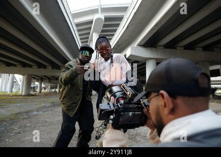 Verschiedene Gruppen von Einzelpersonen, die an Videos der urbanen Szene unter erhöhten Autobahnbrücken teilnehmen, wobei das Kamerateam sich auf die Themen und die Umgebung konzentriert Stockfoto