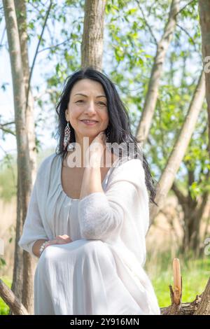 Eine Frau entspannt sich in der Natur des Frühlings, elegant gestellt zwischen Bäumen, in einem weißen Kleid, strahlt Frieden und Harmonie aus, ein beschauliches Porträtkonzept Stockfoto