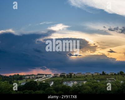 Während die Sonne untergeht, bedeckt ein sanftes warmes Leuchten die Nachbarschaft, während dunkle Sturmwolken hereinrollen und eine markante Balance zwischen Gelassenheit und Impendin schaffen Stockfoto