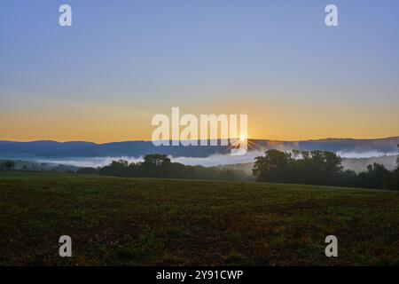 Sonnenaufgang über einem nebeligen Maisfeld mit Hügeln und Bäumen im Hintergrund in ruhiger Atmosphäre, Grossheubach, Miltenberg, Spessart, Bayern, Deutschland, Eu Stockfoto