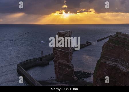 Rote Sandsteinklippe mit lange Anna auf der vorgelagerten Insel Helgoland, Maulwurf als Schutz gegen Erosion, Tölpel, Abendlicht, bewölkter Himmel, Nort Stockfoto