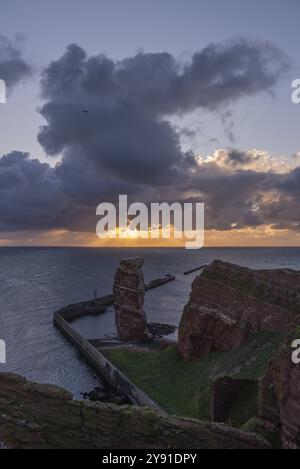 Rote Sandsteinklippe mit lange Anna auf der vorgelagerten Insel Helgoland, Maulwurf als Schutz gegen Erosion, Tölpel, Abendlicht, bewölkter Himmel, Nort Stockfoto