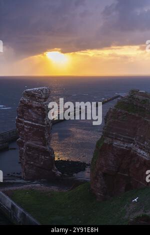 Rote Sandsteinklippe mit lange Anna auf der vorgelagerten Insel Helgoland, Maulwurf als Schutz gegen Erosion, Tölpel, Abendlicht, bewölkter Himmel, Nort Stockfoto