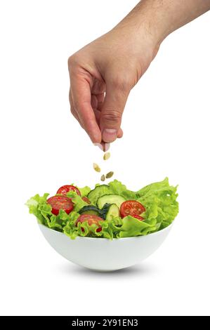 Weiße Schüssel Salat mit frischen Gurken, Tomaten, Eisbergsalatblättern und männliches, von Hand gegossenes Öl mit Löffel über Salat isoliert auf weißem Hintergrund Stockfoto