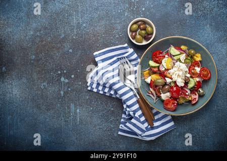 Griechischer frischer, gesunder, farbenfroher Salat mit Fetakäse, Gemüse, Oliven in blauer Keramikschüssel auf rustikalem Betonhintergrund, Draufsicht, mediterrane Würfel Stockfoto