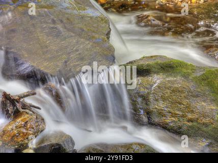 Kleiner Wasserfall, der über moosbedeckte Steine in einem klaren Fluss fließt, lange Exposition Stockfoto