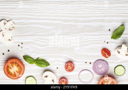 Hintergrund der Speisenzubereitung: Frisch zubereitete Zutaten, Basilikum, Kirschtomaten, Pilze, geschnittene Gurken, Zwiebel, Chili-Pfeffer, Gewürze auf weißem Holzbalken Stockfoto