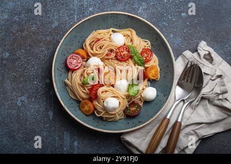 Köstliche Spaghetti mit Mozzarella, farbenfrohe Kirschtomaten, frisches Basilikum auf Keramikplatte auf rustikalem Steinhintergrund mit Blick von oben. Italienisches gesundes Tast Stockfoto