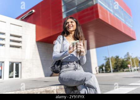 Frau, die ihr Handy benutzt, sitzt auf einer städtischen Bank in einem Gewerbe- und Industriegebiet der Stadt Stockfoto