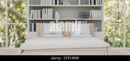 Blick auf ein minimalistisches, sauberes Bett mit weißer Bettwäsche in einem modernen, minimalistischen Schlafzimmer mit Bücherregal und großen Fenstern mit Blick auf die Natur. Stockfoto