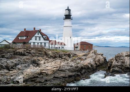 Das Portland Head Light steht hoch an einer felsigen Küste mit Blick auf das Meer. Die Leute laufen entlang des Weges in der Nähe des Leuchtturms und des Wächterhauses. Stockfoto