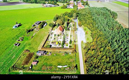 Üppiges grünes Gras und Bäume umgeben eine Kirche und einen Friedhof in der deutschen Landschaft. Eine Schotterstraße führt zur Kirche und führt an einem kleinen für vorbei Stockfoto