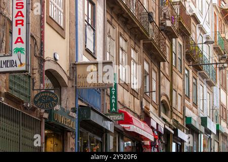 Farbige Fassaden mit Fliesen in porto mit Werbeschildern an der Wand, Stahlbalkons darüber. Stockfoto