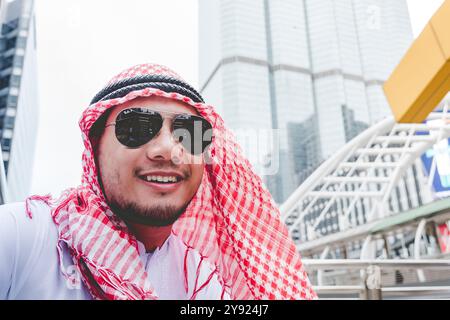 Hübscher moderner arabischer Mann, der in der modernen Stadt steht, trägt muslimische Kleidung Kopftuch östliches ethnisches Lächeln vor dem Büro. Ein arabischer Mann sucht ein neues Projekt Stockfoto