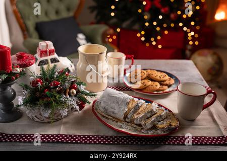 Weihnachtstisch mit Stollenkuchen, Tassen, Keksen auf dem Hintergrund von dekoriertem Weihnachtsbaum und Kamin, gemütliche Weihnachtsatmosphäre Stockfoto