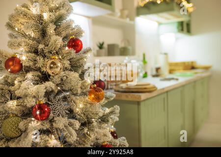 Wunderschön dekorierter Weihnachtsbaum mit roten und goldenen Ornamenten, beleuchtet von warmweißen Lichtern. Im Hintergrund befindet sich eine gemütliche Küche mit festlichem d Stockfoto