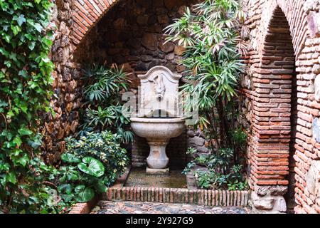 Malaga, Spanien - 29. April 2017: Ein ruhiger Innenhof mit einem alten Brunnen, eingebettet in üppiges Grün. Stockfoto