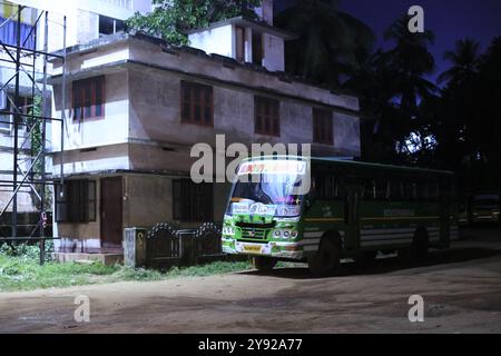 Eine ländliche Straße in der Nacht, mit einem grünen Bus, der in der Nähe eines ruhigen Gebäudes parkt und von Straßenlaternen in einer ruhigen Gegend beleuchtet wird. Stockfoto