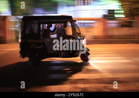 Nächtliche Schwenkaufnahme einer Auto-Rikscha, die auf einer Stadtstraße rasant fährt, wobei Bewegungsunschärfe ihre Bewegungen einfangen. Stockfoto