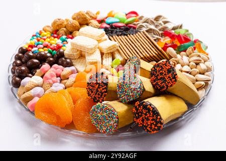 Eine bunte Auswahl an Snacks mit getrockneten Früchten, Waffeln, Pistazien, Süßigkeiten und dekorierten Bananen, ideal für Partys oder festliche Leckereien Stockfoto