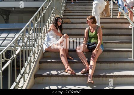 Porto, Portugal - 12. September 2024 : zwei Frauen unterhalten sich, während sie auf einer Treppe in einer lebhaften Gegend sitzen. Stockfoto