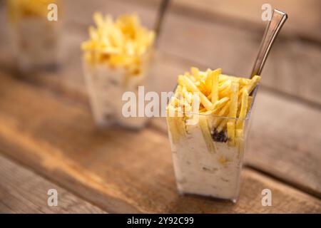 Frische Pommes Frites auf cremigem russischen Salat in klaren Tassen, rustikaler Holzhintergrund, Gourmet-Vorspeise Stockfoto