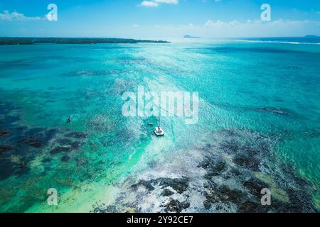 Toller Blick aus der Luft auf einen modernen Katamaran vor der Insel L'îlot Bernache, Mauritius, umgeben von Korallenriffen und schwarzen vulkanischen Felsen Stockfoto