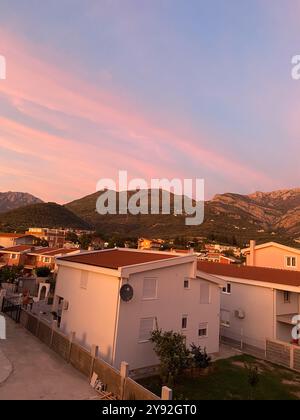 Der lebhafte Sonnenuntergang überzieht Wohngebäude in warmen Tönen und schafft einen atemberaubenden Kontrast zum Abendhimmel. Friedlicher Übergang von Tag zu Nacht Stockfoto