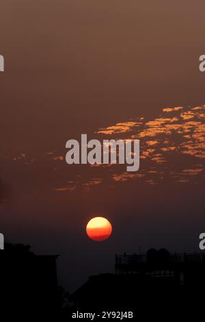 Eine faszinierende goldene Stunde Sonnenuntergang mit einer brennenden orange Sonne und verstreuten Wolken über Dehradun City, Uttarakhand, Indien, fängt die ruhige Stadtlandschaft ein Stockfoto