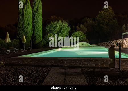 Beleuchteter Swimmingpool auf dem Hügel von Montemassi, umgeben von Zypressen und Oleandern in der Provinz Grosseto. Italien Stockfoto