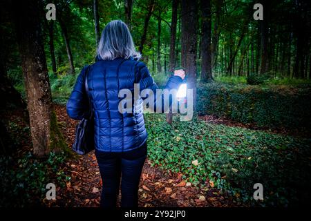Reife Frau mit Laterne im Wald in der Dämmerung, Chenonceau Woods, Frankreich. Stockfoto
