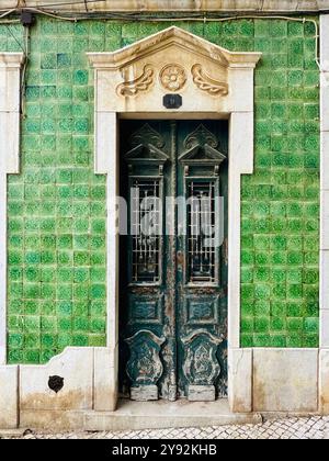 Alte verwitterte grüne Tür umgeben von Keramikfliesen an der Algarve, Portugal Stockfoto