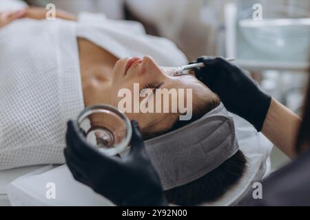 Eine Kosmetikerin führt eine Gesichtspeelbehandlung bei einer jungen Frau durch, wobei der Schwerpunkt auf Hautverjüngung und Pflege in einem professionellen Schönheitssalon liegt Stockfoto