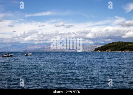 Blaues Wasser des Ionischen Meeres im Nordosten der Insel. Berge in Albanien am Horizont. Blauer Himmel mit weißen Wolken. Agios Spyridon, Co Stockfoto