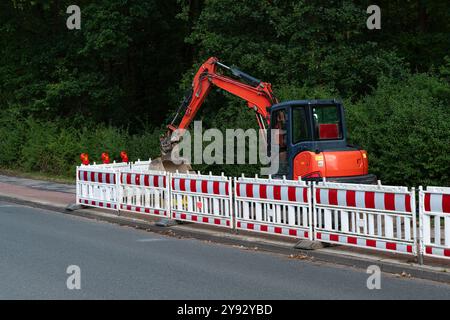 Ein Baupersonal gräbt am Abend mit einem Bagger in der Nähe eines bewaldeten Gebiets entlang der Straße. Zum Schutz des Standorts und der Passanten sind Sicherheitsbarrieren eingerichtet. Stockfoto