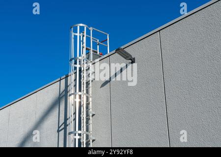 Eine stabile Metallleiter erstreckt sich vom Boden bis zum Dach eines Gebäudes und reicht zu einem klaren blauen Himmel ohne Wolken, was einen sonnigen Tag und die städtische Architektur hervorhebt. Stockfoto