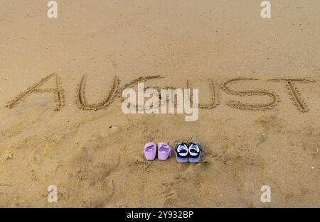 Handgeschriebener Text für die Ankündigung des Babys im august ist auf dem Strand. Sauberes Wasser und kleine Wellen sind im Hintergrund Stockfoto